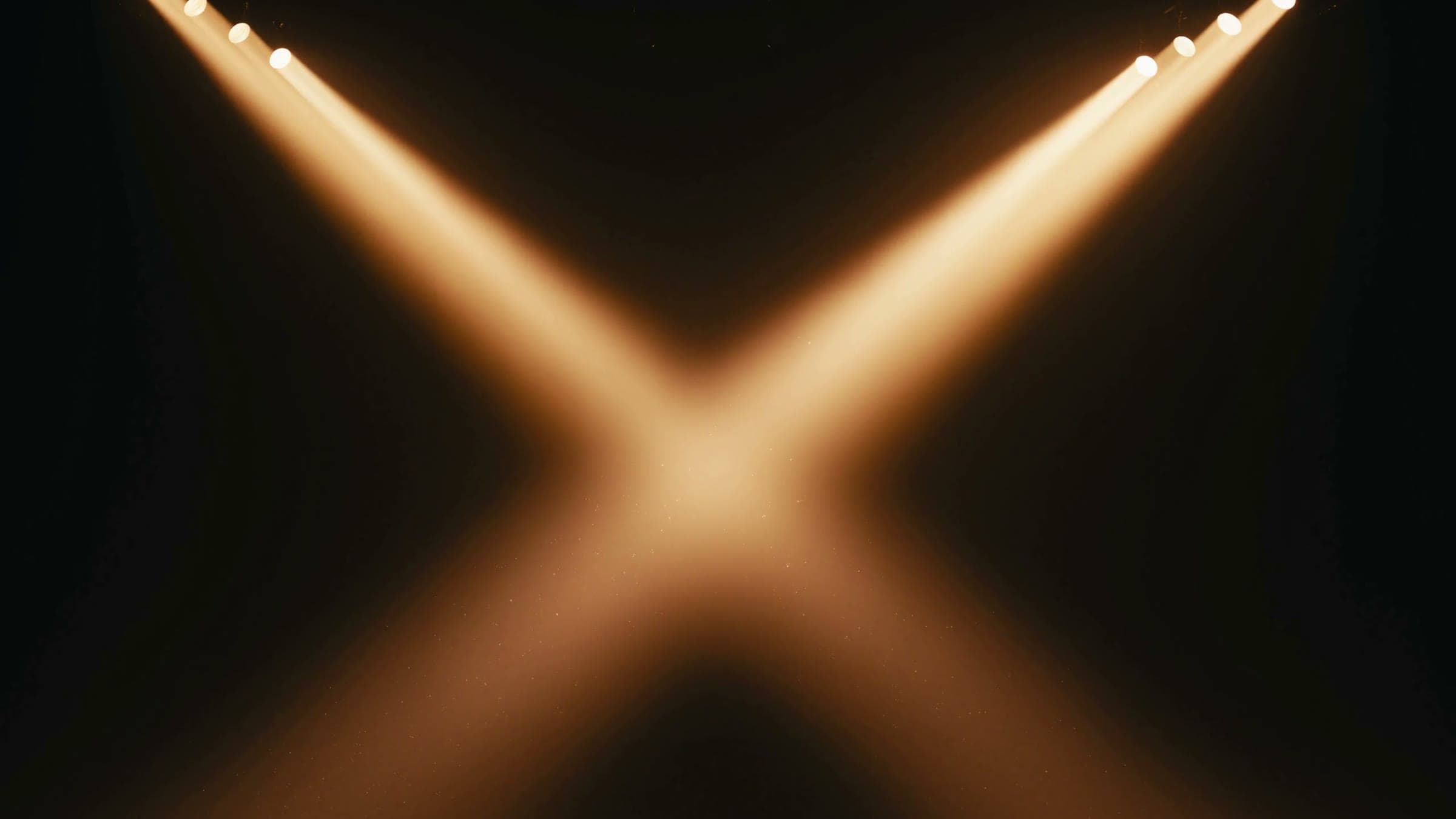 Two beams of warm light crossing into an X in a dark hall.