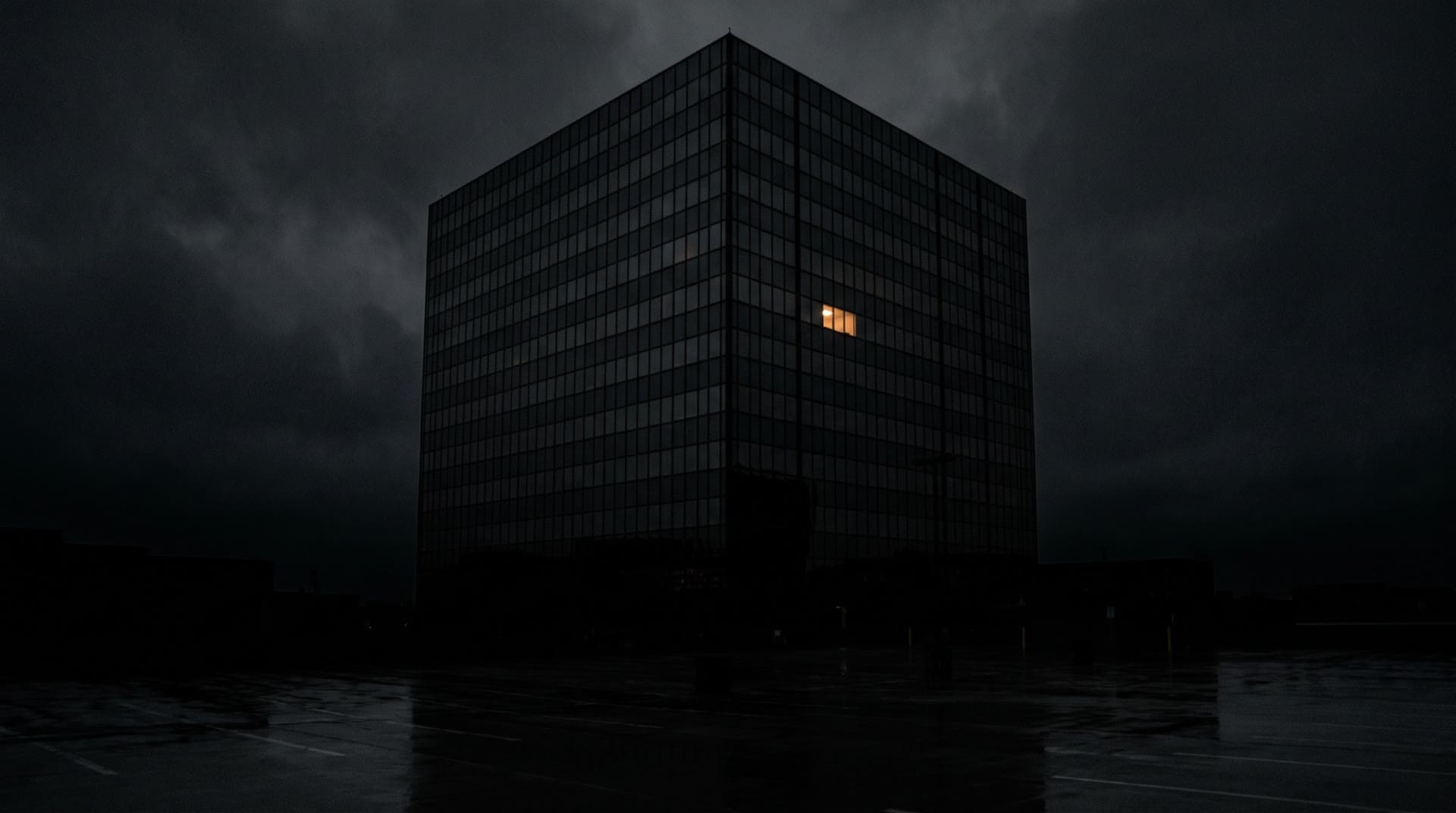 A dark office tower at night with a single lit window.