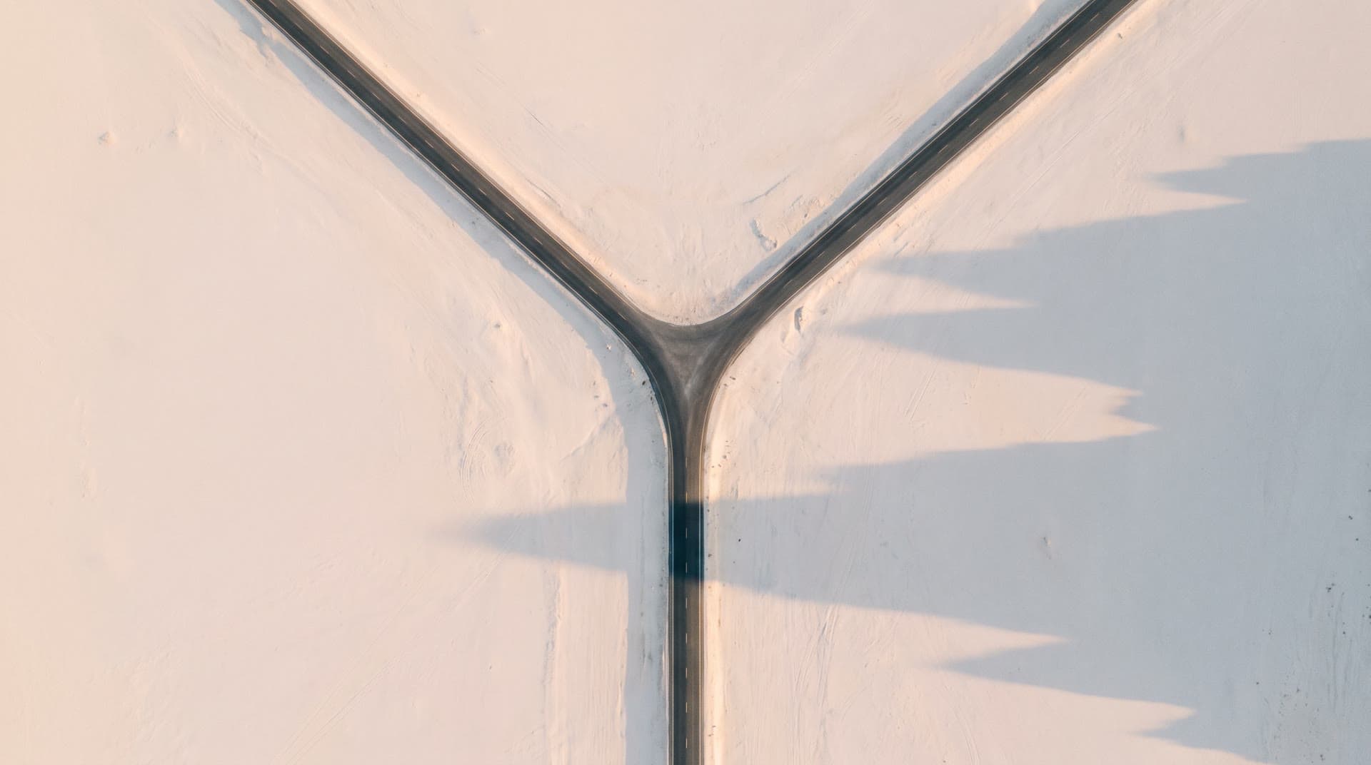 A road seen from above, splitting in two across pale ground.